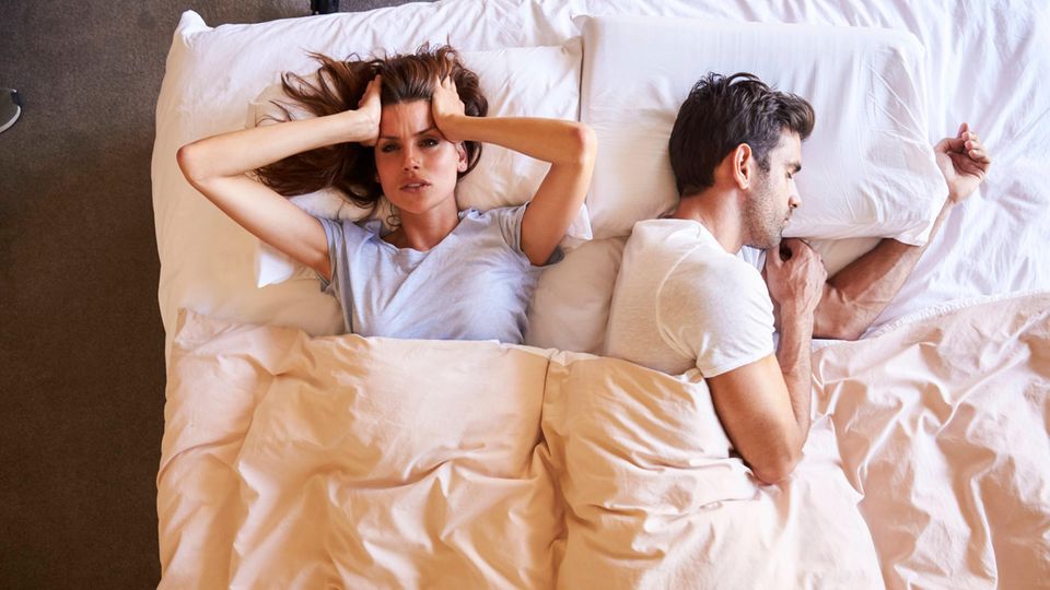 Sleepless woman lies in bed next to a man