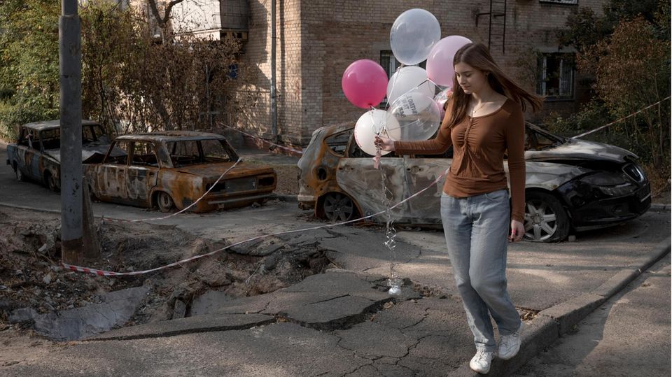 Alltag in Kiew: Eine Schülerin geht nach ihrer bestandenen Uni-Aufnahmeprüfung nach Hause – vorbei an aufgerissenen Straßen und ausgebrannten Autos, Spuren eines russischen Drohnenangriffs Wochen zuvor