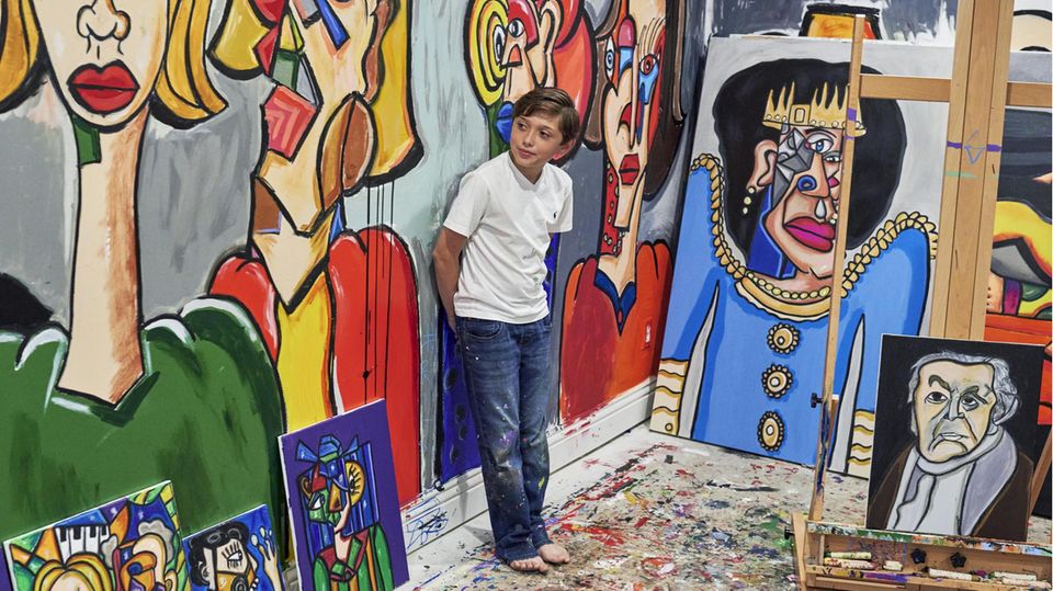 Ten-year-old Andres Valencia is standing in a room with many of his paintings