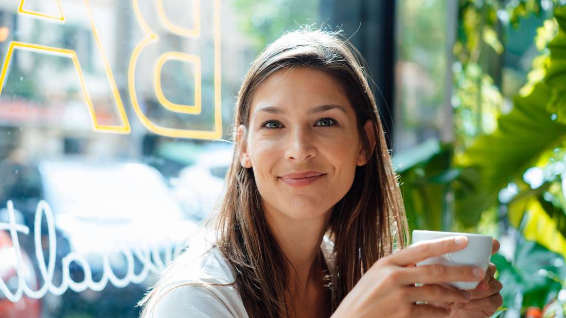 Woman drinking coffee and smiling at the camera. 