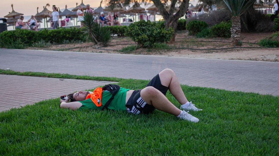 A drunk party tourist lies on the lawn on the beach in Mallorca