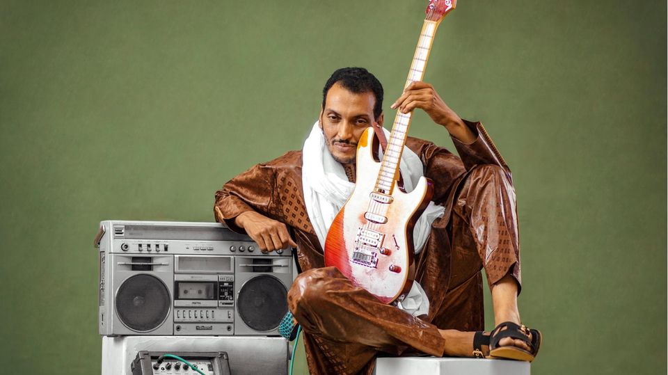 A man sits next to a stereo with an electric guitar