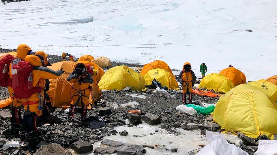 Mountaineers in thick jackets stand between abandoned tents in the base camp on Mount Everest. There is snow in the background