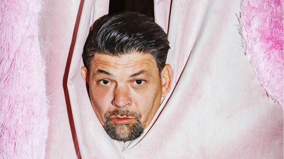 Tim Mälzer's head looks through a pink curtain