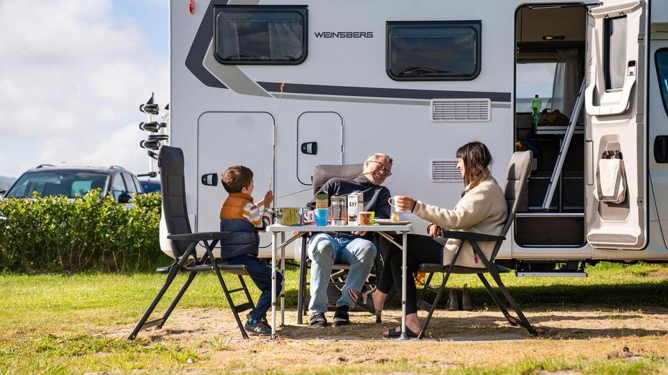 Editor Gunnar Herbst, his wife and their son are sitting at a camping table in front of their motorhome and eating