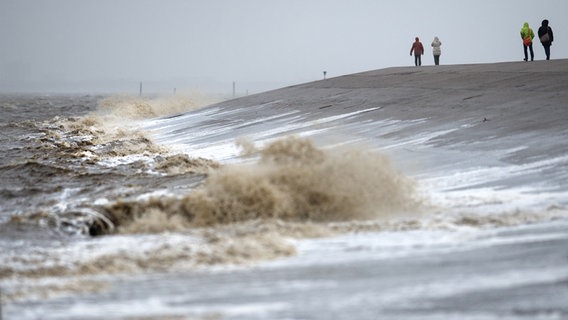 Walkers walk on the dike in Norddeich, where the waves are hitting.  © picture alliance Photo: Matthias Balk