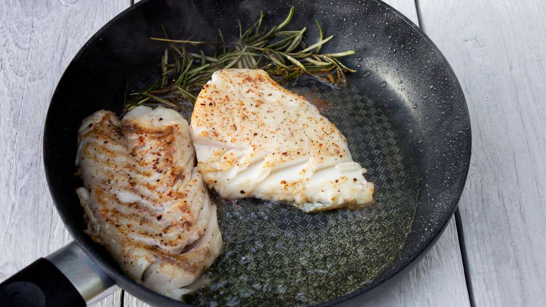 Cod fillet with rosemary sprig in the frying pan.
