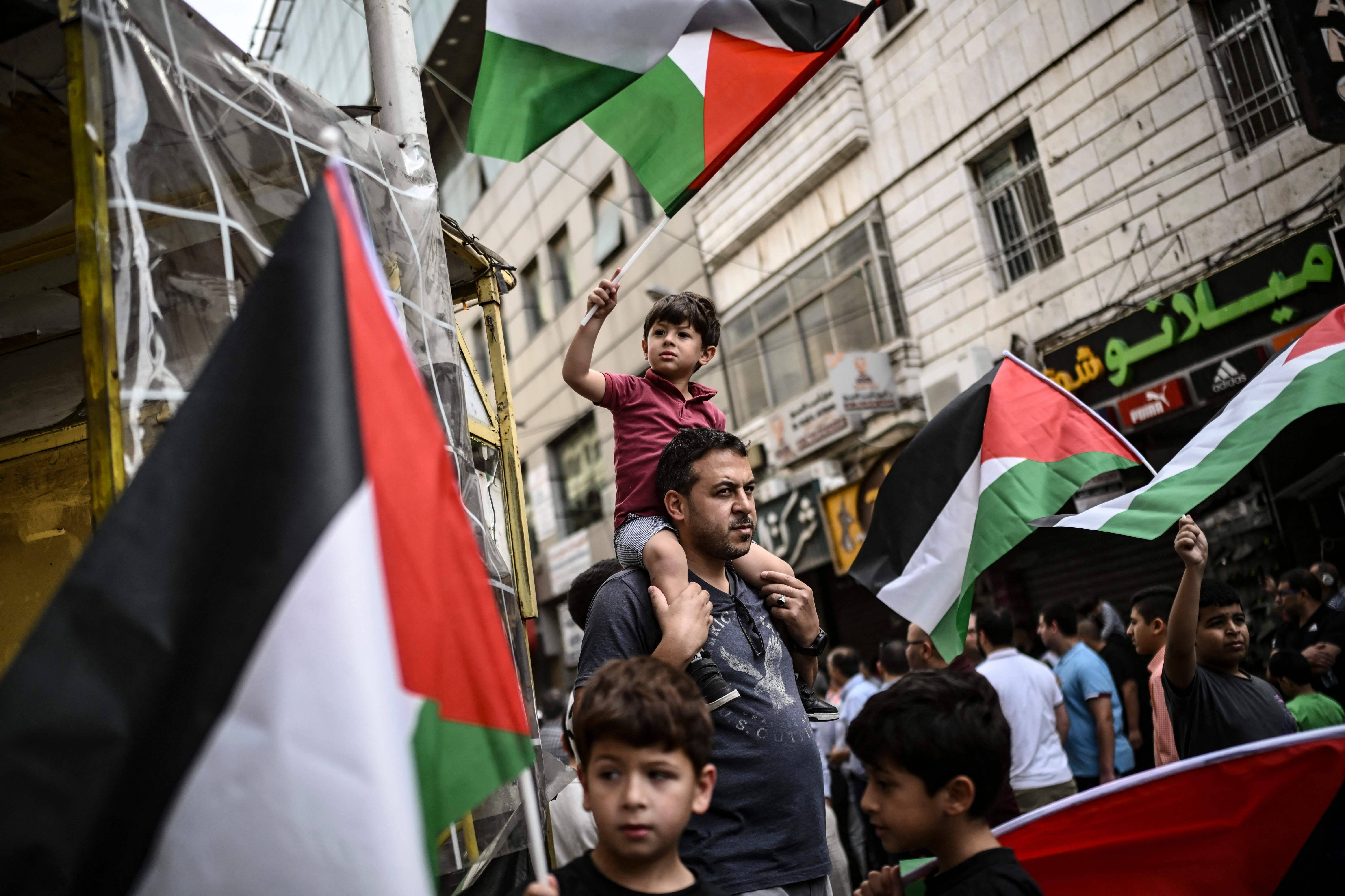 Un homme porte un enfant sur ses épaules tandis que des personnes agitent des drapeaux nationaux palestiniens lors d'une marche de solidarité avec la population de la bande de Gaza, dans la ville de Ramallah en Cisjordanie occupée, le 27 octobre 2023. — © ARIS MESSINIS / AFP