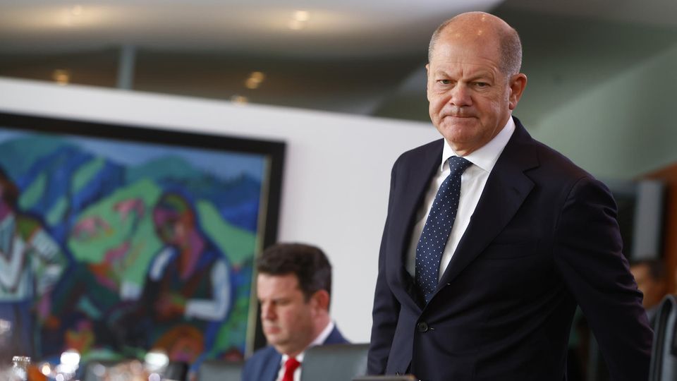 Chancellor Olaf Scholz at a cabinet meeting.  A man in a suit and tie stands at a table