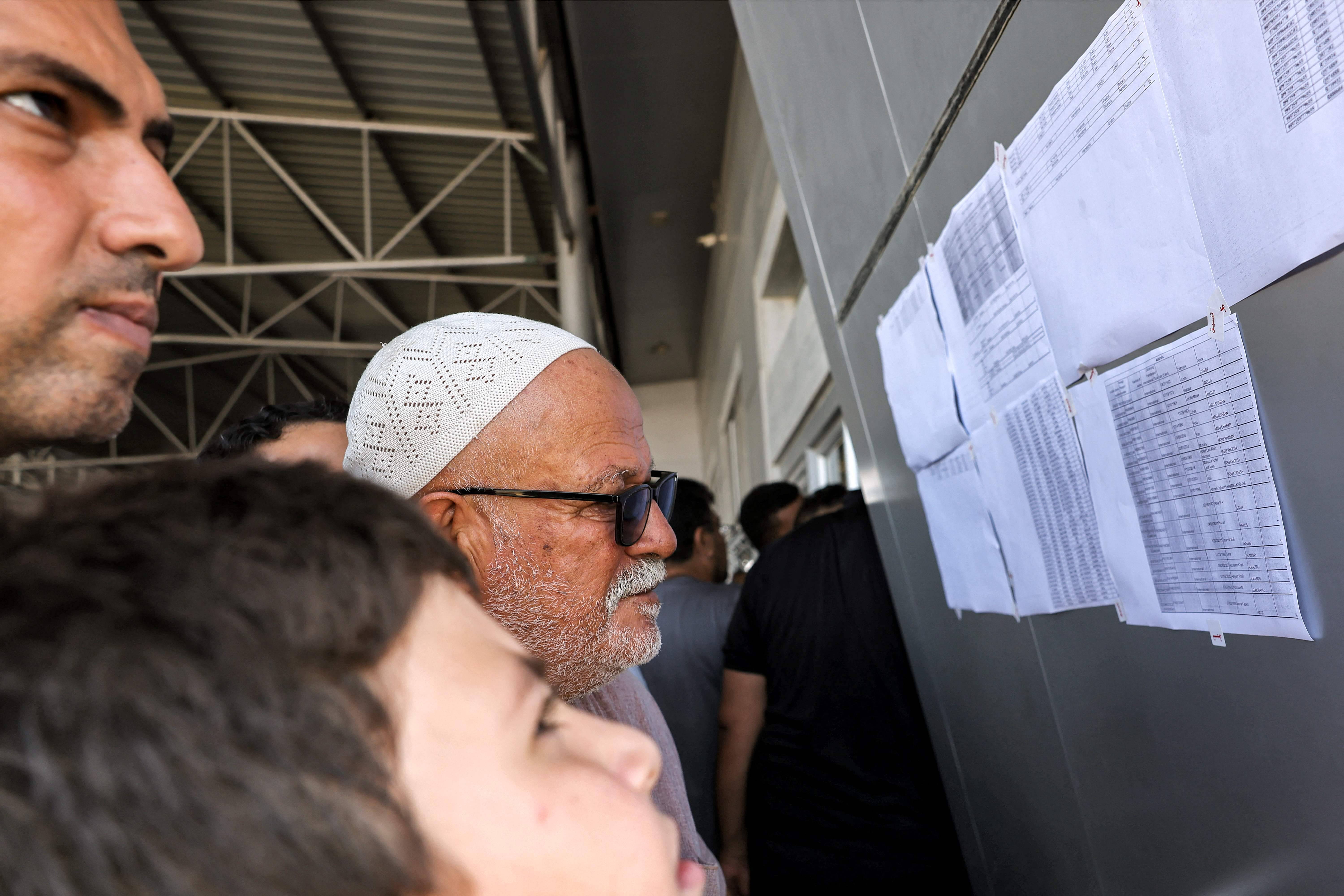 Des personnes contrôlent si leur nom apparaît dans la liste des personnes autorisées à traverser le poste de Rafah. — © MOHAMMED ABED / AFP