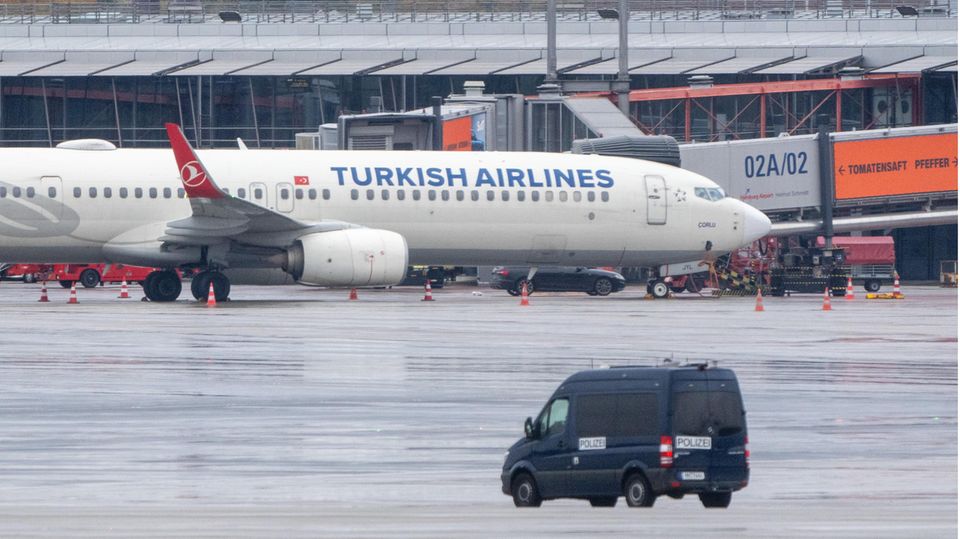 A police vehicle is parked at the airport in front of a plane with a car with a hostage taker parked next to it