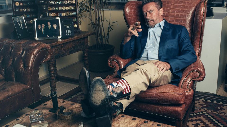 Portrait of Arnold Schwarzenegger with cowboy boots and cigar in a leather armchair