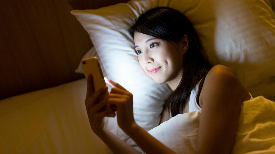 A woman lies in bed and types on her smartphone