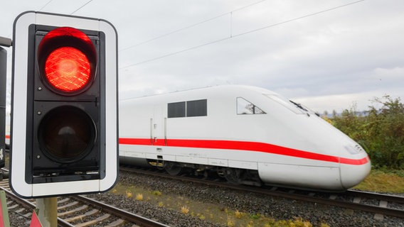A red traffic light lights up at a level crossing in front of an ICE train.  © dpa Photo: Julian Stratenschulte