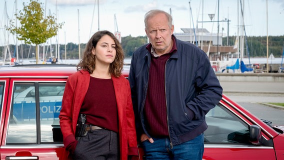 Mila Sahin (Almila Bagriacik), Klaus Borowski (Axel Milberg) stand in front of a red car.  © NDR Photo: Christine Schroeder