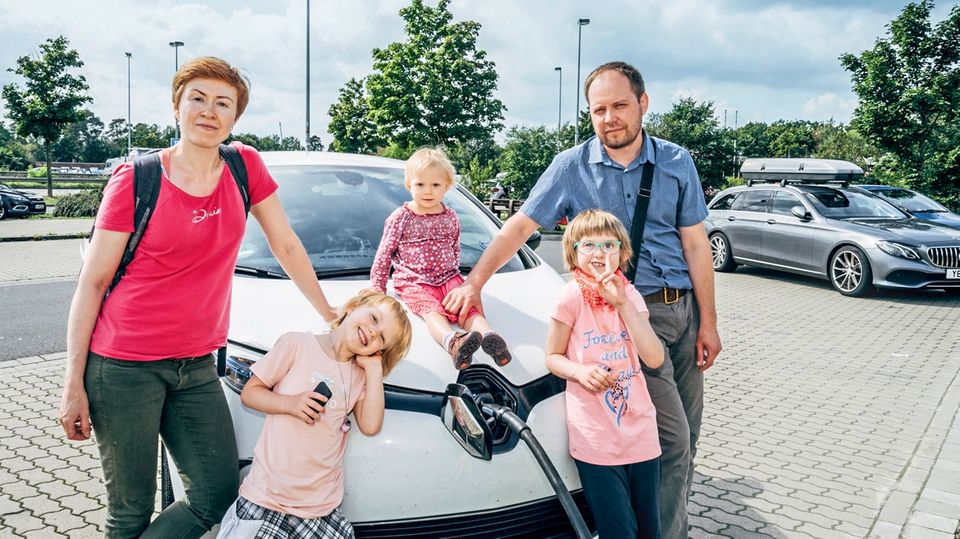 Parents with three children stand in front of an electric car that is being charged