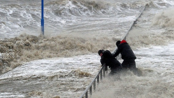 Two men hold on to a railing on the storm-washed waterfront in Dagebüll © picture alliance / dpa Photo: Carsten Rehder