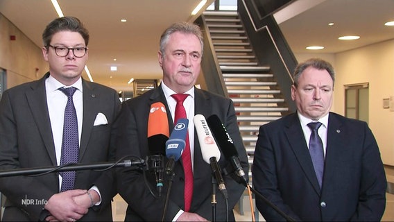 The chairman of the GDL, Claus Weselsky, and two other men stand in front of several microphones.  © Screenshot 