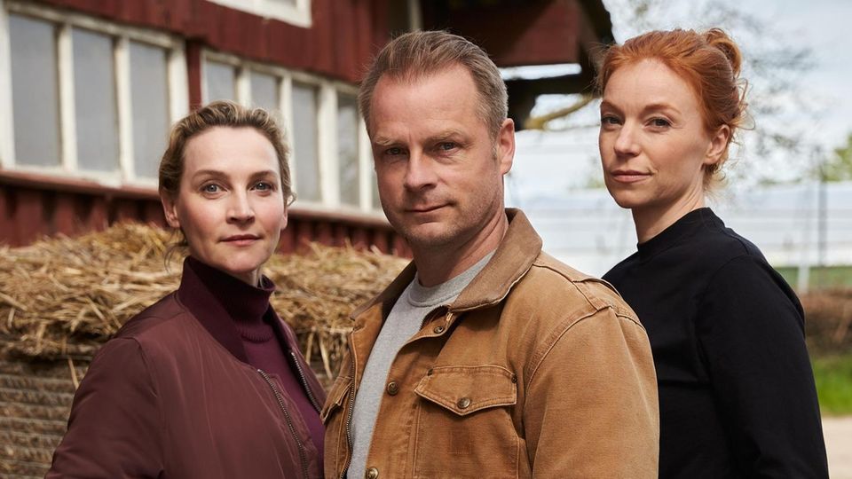 Three actors pose in front of a barn