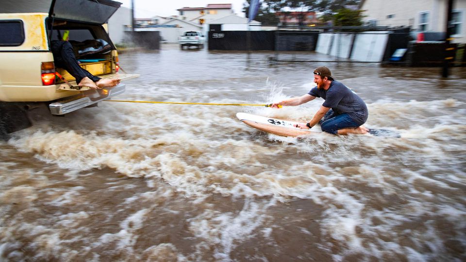 Ein Mann lässt sich Anfang Januar auf einem Surfbrett durch die überfluteten Straßen Santa Barbaras ziehen