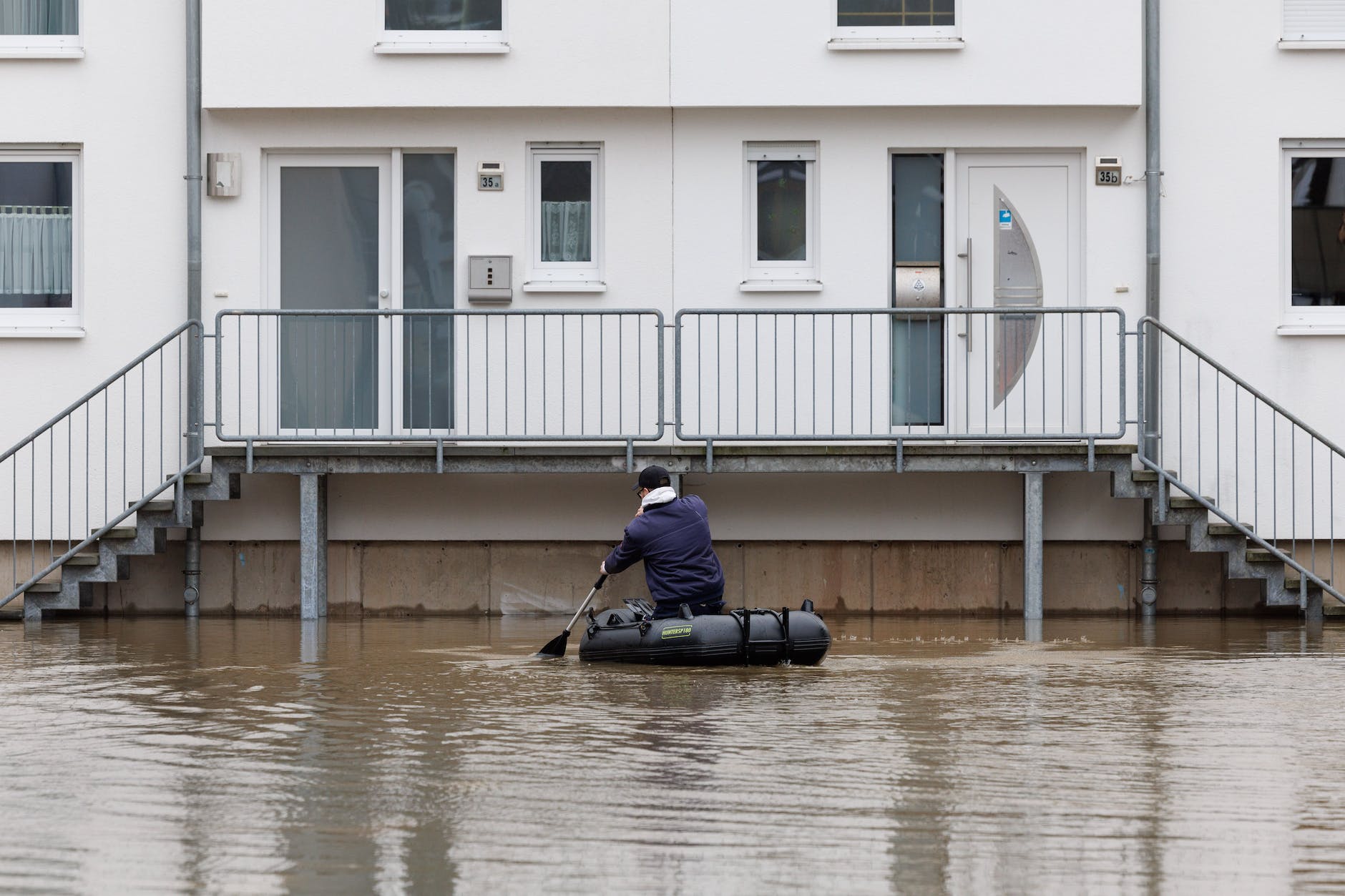 North Rhine-Westphalia, Beverungen: A man sits in an inflatable boat and paddles to a house that is in the water.