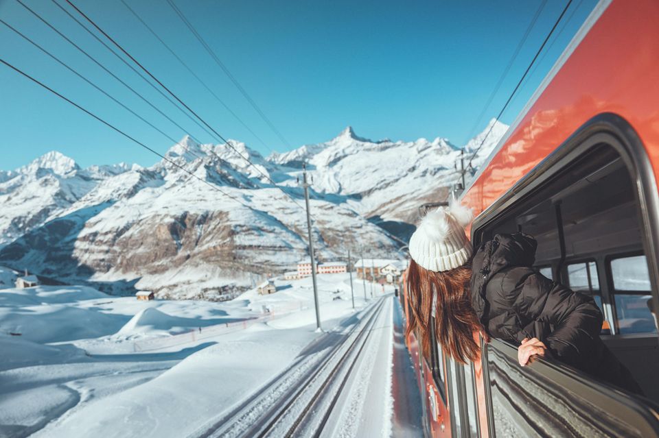 A woman looks out the window of a train in a snowy mountain landscape