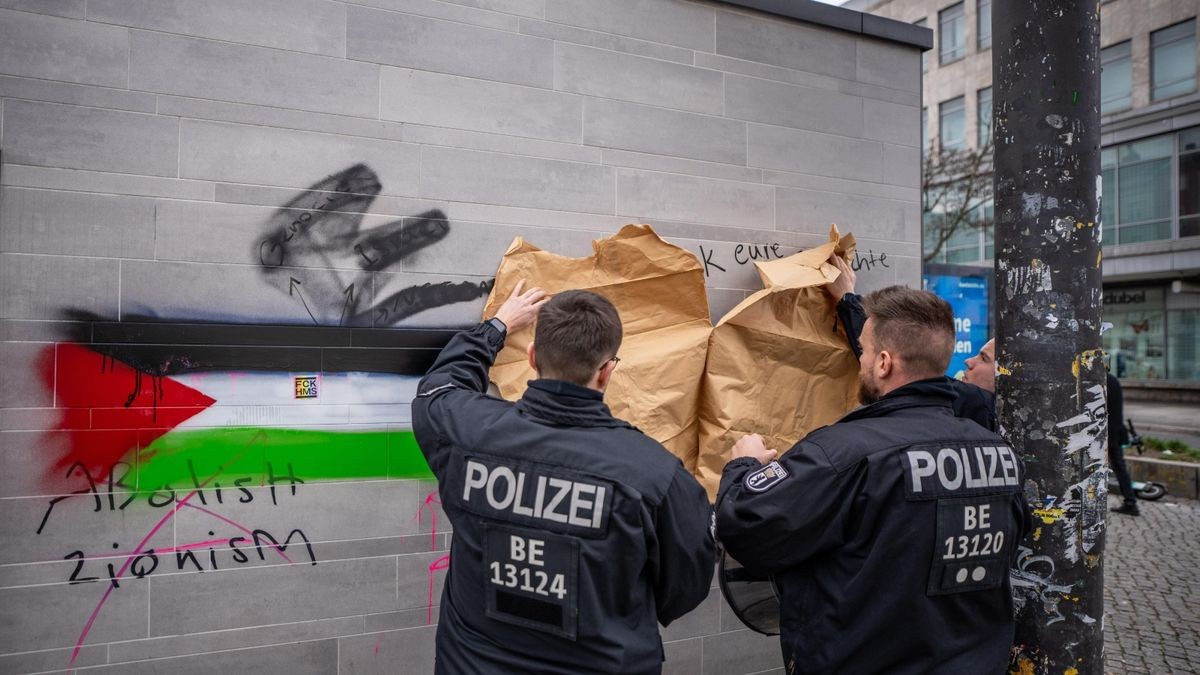 Polizisten kleben eine Israel-feindliche Schmiererei vor einer Propalästinensischen Demonstration am Hermannplatz in Berlin mit Neukölln mit Papier ab.