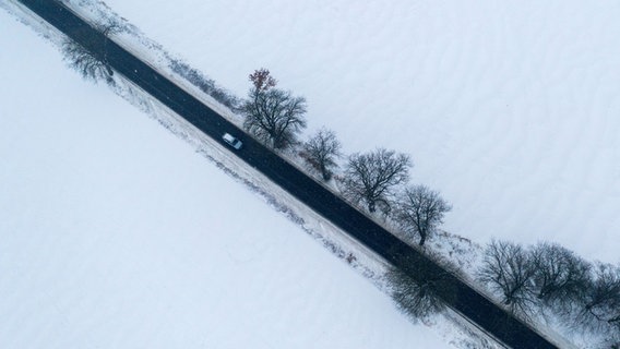 An aerial view shows a car driving on a cleared road through a snowy winter landscape.  © picture alliance/dpa |  Jens Büttner 