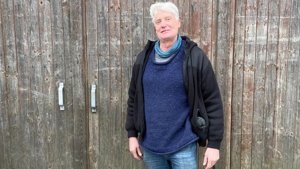 A man with white hair and a fleece jacket stands in front of a barn door.