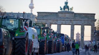 Numerous tractors are parked in front of the Brandenburg Gate during a farmers' protest on the Straße des 17. Juni.