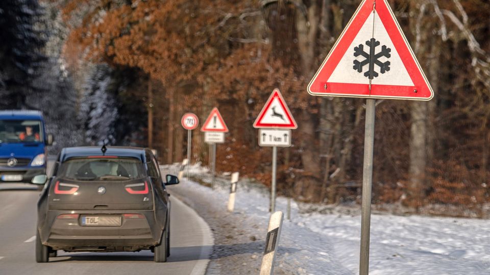 A car drives past a traffic sign warning of slippery snow or ice