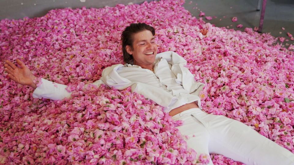 Fragrance influencer Jeremy Fragrance lies on a pile of rose petals