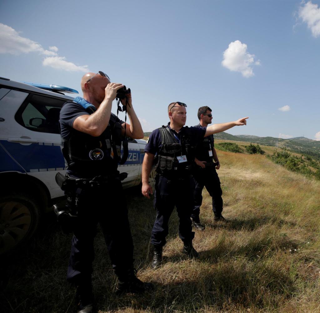 A member of the European Border and Coast Guard Agency (FRONTEX) points his finger as his colleague uses binoculars during a patrol near Albania-Greece border, in Kapshtica near Korce, Albania, July 23, 2019. Picture taken July 23, 2019. REUTERS /Florion Goga - RC116FDD1A10