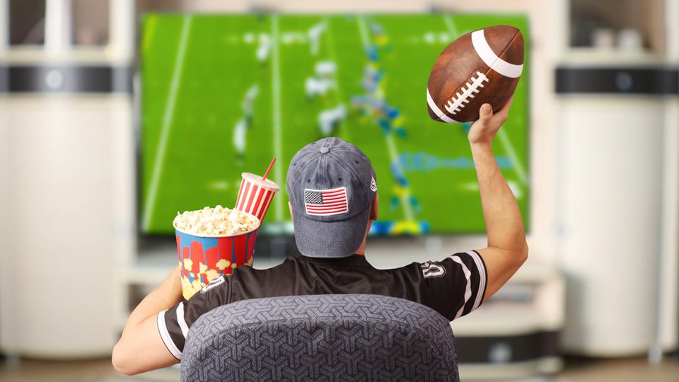 Super Bowl Gadgets: Football fan sits in front of a television with a ball and popcorn