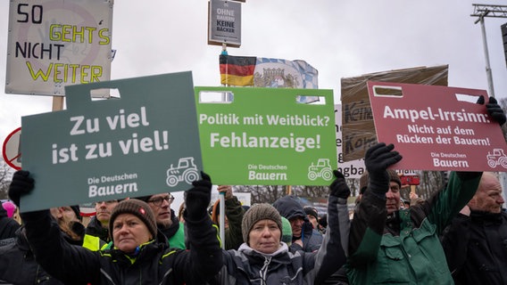 At a large rally in Berlin, some farmers hold up protest signs.  © dpa Photo: Monika Skolimowska