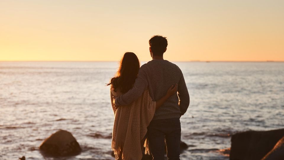 A couple stands on the seashore and looks into the sunset.