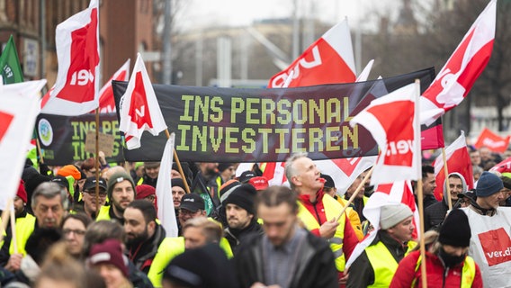 Participants in a Verdi demonstration walk through the city center of Hanover with a banner that reads “Invest in personnel”.  © Michael Matthey/dpa Photo: Michael Matthey