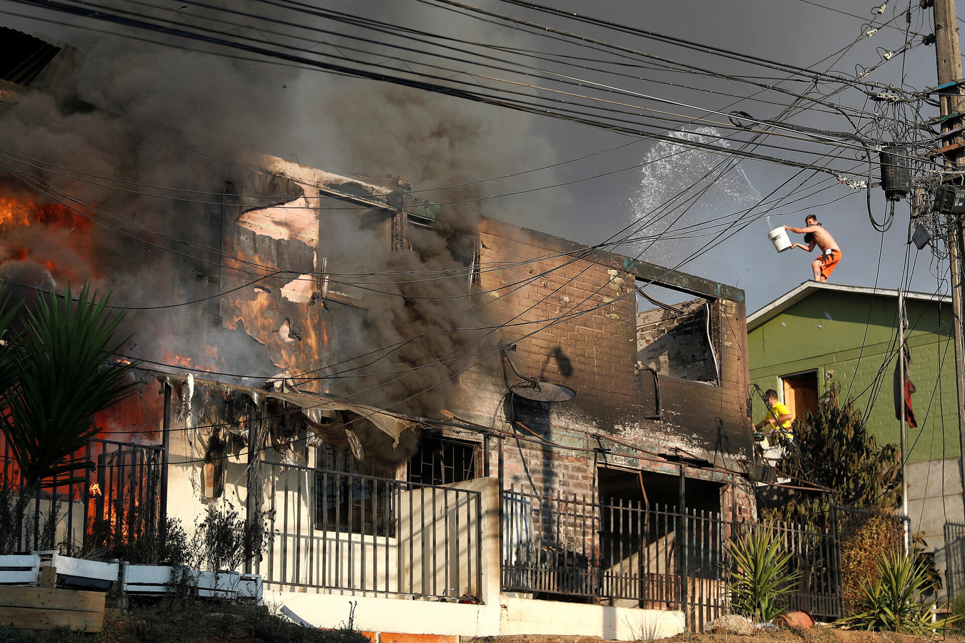 Residents try to put out a fire devastating a house in Vina del Mar, Chile, February 3, 2024. 