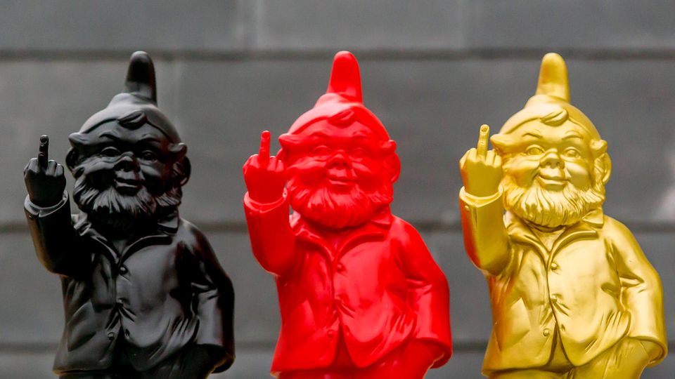 Three garden gnomes in the colors of the German flag stand next to each other and raise their middle fingers