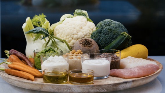 Various healthy foods such as vegetables, yogurt and oils stand or lie on a wooden plate.  © NDR 