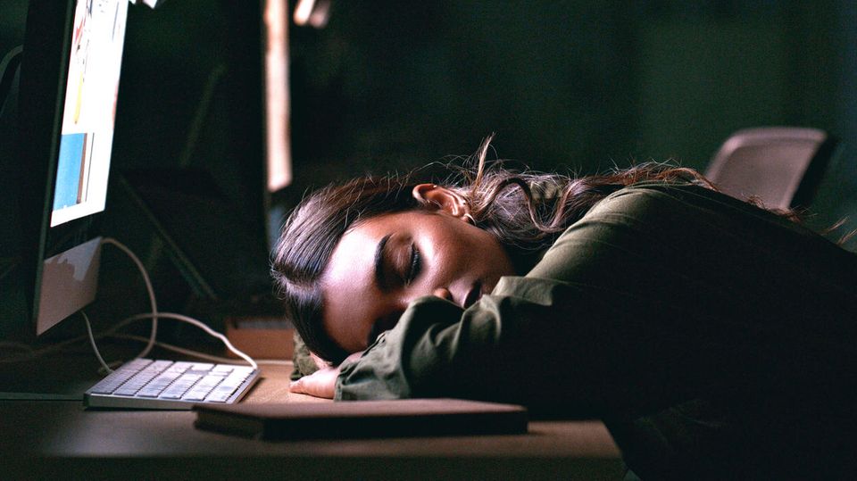 A woman sits exhausted in front of the laptop.