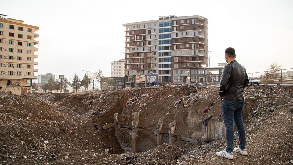 A young man stands at a hole in the ground in a city in Turkey that was destroyed by the earthquake