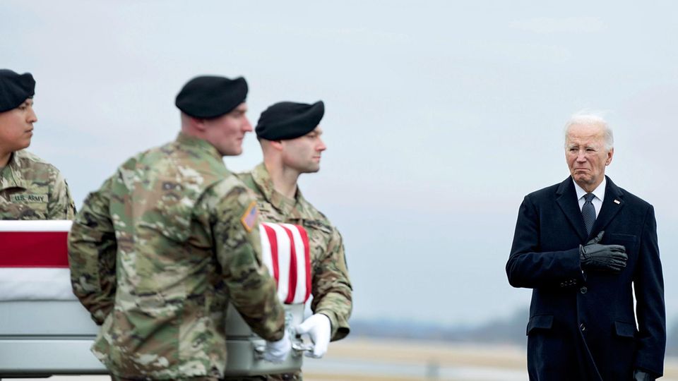 Biden next to a coffin carried by soldiers