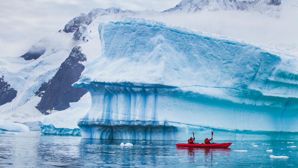 People paddling a kayak near an iceberg in Antarctica