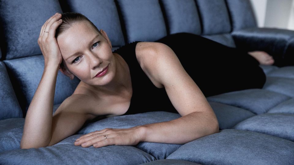 Portrait of Sandra Hülser, in a black dress, lying on a blue sofa