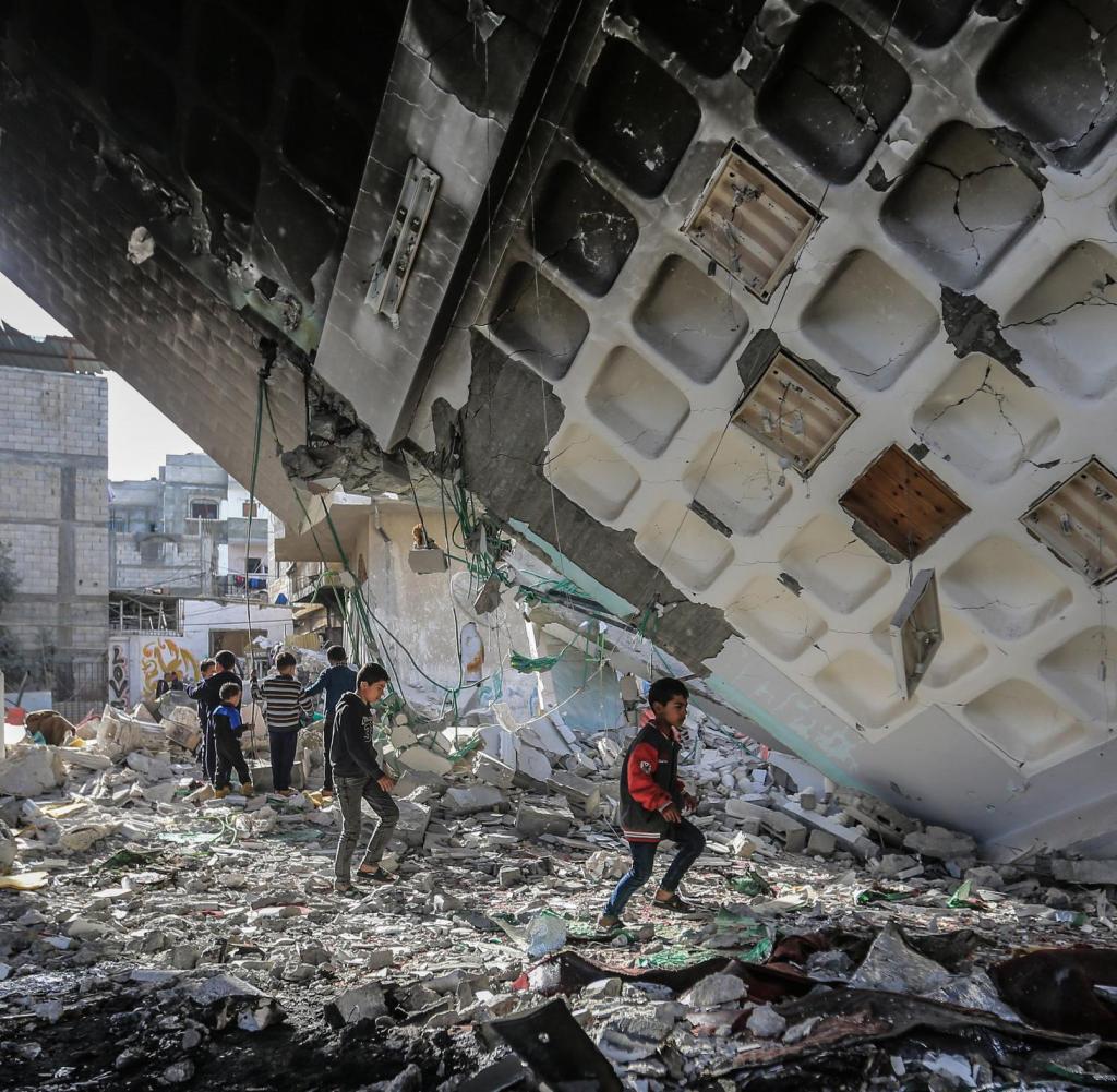12.02.2024, Palästinensische Gebiete, Rafah: Palästinensische Kinder gehen unter den Überresten der Al-Huda-Moschee, die nach einem israelischen Luftangriff zerstört wurde. Foto: Mohammed Talatene/dpa +++ dpa-Bildfunk +++