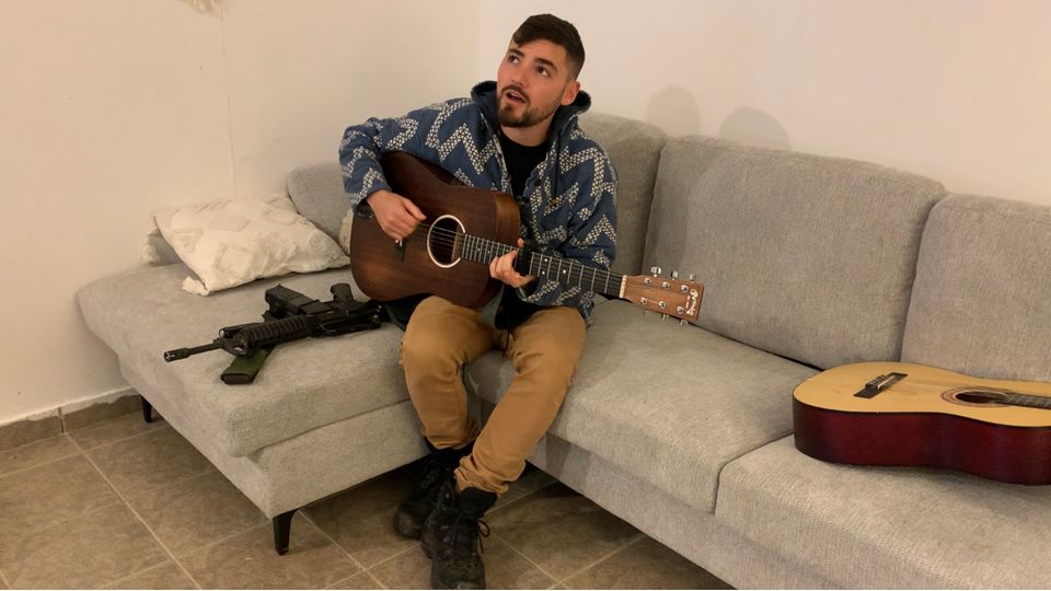 Omri Goren at home in Jerusalem.  The 28-year-old is a singer and has been deployed as a reservist in the army since October 7th.  Machine guns and guitars are his constant companions