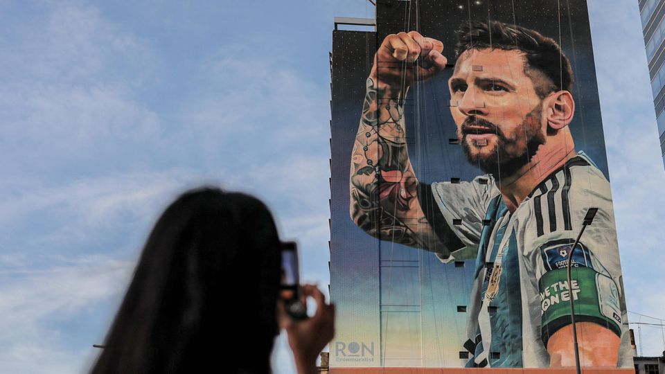 Lionel Messi as a picture on a house wall, a woman photographs him.
