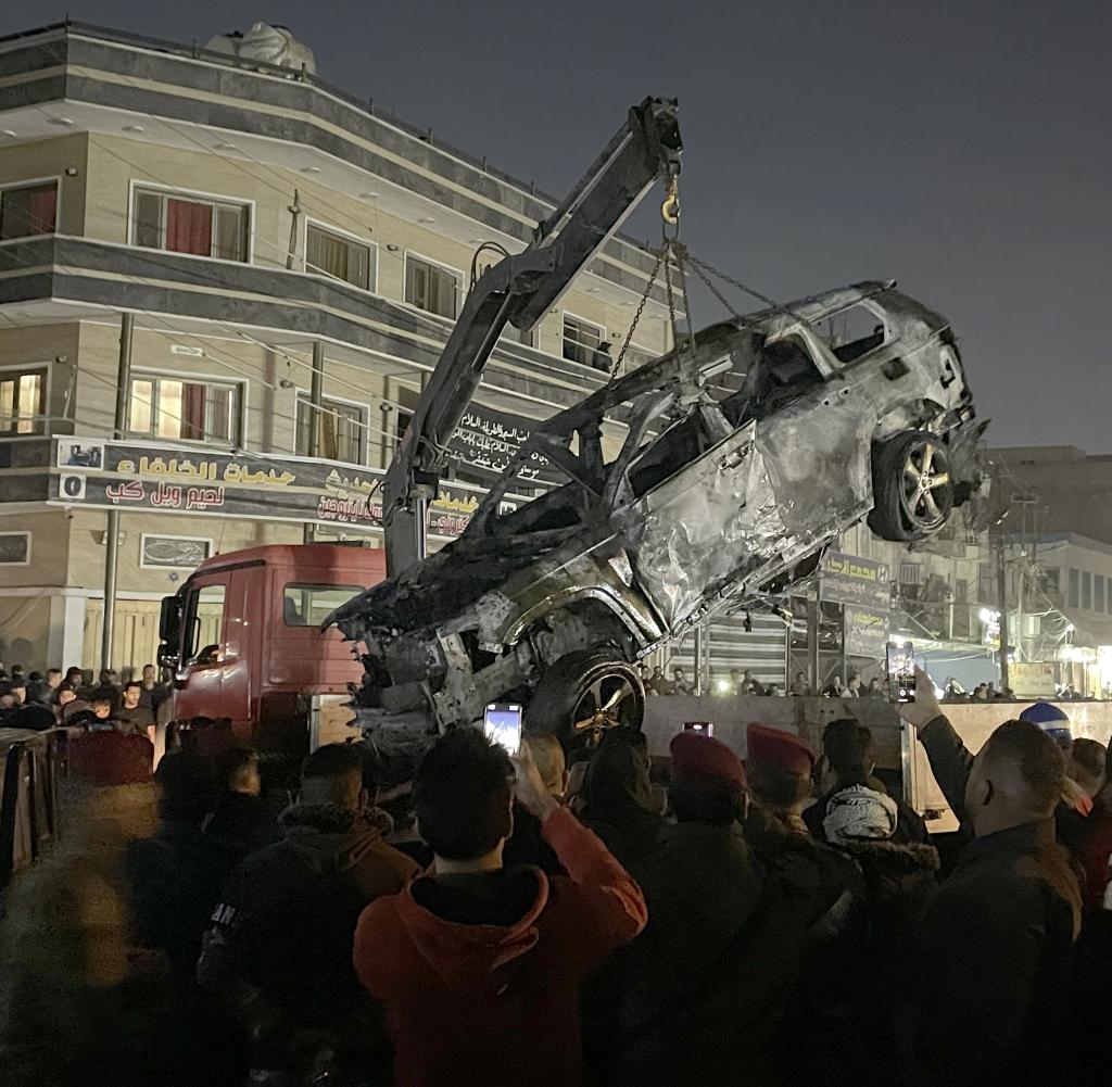 A burned-out car is lifted by a crane.  The commander is said to have sat in this car