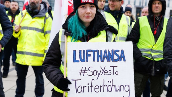 An employee holds a sign with the inscription Lufthansa #SayYesTo tariff increase at a rally by the Lufthansa Technik division in front of the departure hall in Terminal 1 of BER Airport.  © Carsten Koall/dpa 